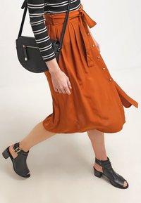Rust-orange midi-nederdel lavet af glat stof, med frontknapper og bindebånd i taljen. Kombineret med sorte åben-tå hæle sandaler.