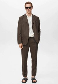 Brun jakkesæt med et notch-lapel, parret med en hvid polo. Sorte solbriller og sorte sandaler fuldender looket. Glat stof, skræddersyet pasform.