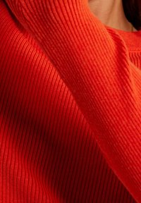 Pull en maille côtelée rouge avec des manches longues, un col rond et une texture douce, présentant un motif continu sur l'ensemble.