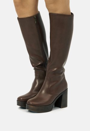 Bottes marron montantes en matériau synthétique lisse, avec une fermeture éclair sur le côté, des talons empilés robustes et un design à bout rond.