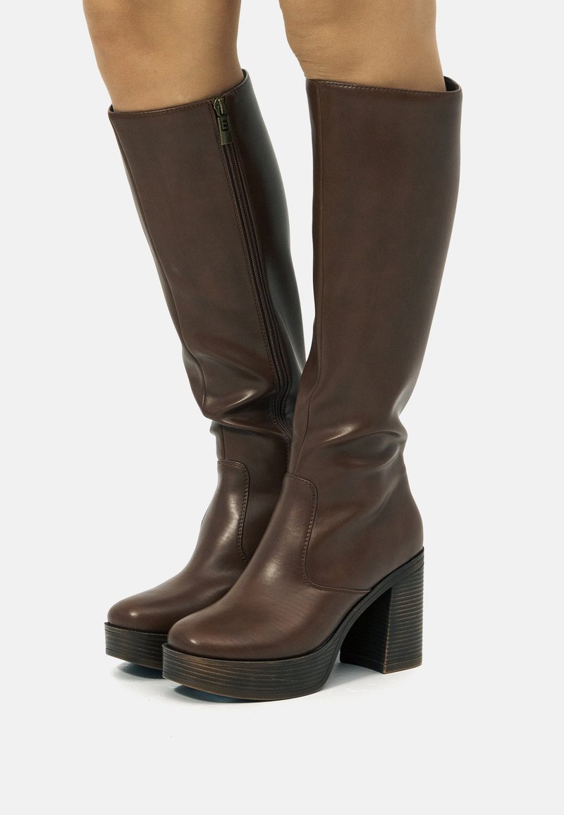 Botas marrones hasta la rodilla hechas de material sintético suave, con cremallera lateral, tacones gruesos y apilados, y un diseño de punta redonda.