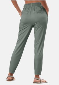 Green, lightweight pants made of smooth fabric with a relaxed fit, elastic waistband, and two back pockets. Paired with flat sandals.