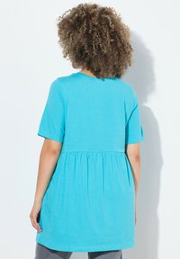 Tunic turchese con maniche corte e vita raccolta. Realizzata in tessuto leggero e morbido con una texture liscia.