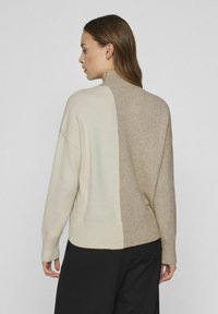 Gebreide trui met een hoge nek, voorzien van een kleurblokontwerp in crème en beige. Geribde manchetten en zoom; zachte textuur.