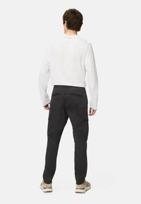 Sorte cargo bukser med sidelommer og lige ben, parret med en hvid langærmet skjorte og beige sneakers.