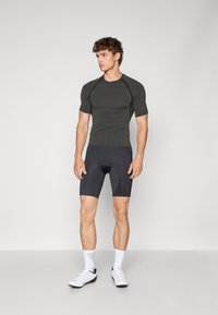 Tætsiddende mørkegrå kortærmet træningstop med ribbet tekstur, sammen med sorte cykelshorts. Modellen har hvide træningssko og sokker på.