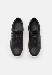Paire de baskets en cuir noir Calvin Klein avec des lacets noirs et des semelles en caoutchouc blanches, vue de dessus sur un fond blanc.