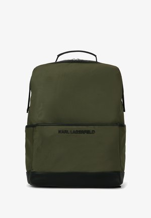 Oliwkowy plecak z nylonu z czarnymi skórzanymi akcentami, górną rączką, logo z przodu i podwójnymi suwakami. Posiada dwie boczne kieszenie.