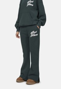Ciemnozielony bawełniany sweatshirt z kapturem i kieszenią kangurką, w połączeniu z dopasowanymi spodniami dresowymi z białym napisem "Good for Nothing".