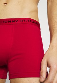 Punaiset puuvillabokserit, joissa on musta "TOMMY HILFIGER" -logolla varustettu joustava vyötärö, ja jotka ovat muotoilultaan istuvat ja pinnaltaan sileät.