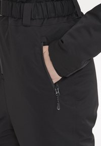 Svarta skidbyxor med en mjuk textur, med elastisk midja och blixtlåsficka på sidan, som visar en smidig design.