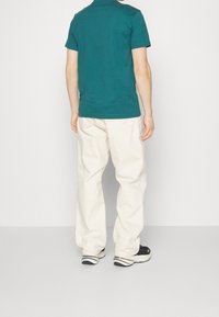 Turkusowa bawełniana koszulka w połączeniu z kremowymi, luźnymi spodniami. Czarne buty z białymi i szarymi akcentami. Prosty, casualowy design.