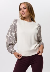 Lichtbeige sweatshirt met gegraveerde pofmouwen in bruine lijnen. Heeft een geribde halslijn en zoom, dynamisch ontwerp en een zachte textuur.
