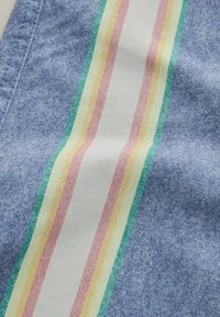 Tissu bleu avec une couture cousue et une bande blanche verticale présentant des lignes parallèles vertes, jaunes et roses.