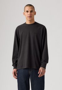 T-shirt a maniche lunghe nera in cotone con collo a girocostato e logo discreto sul petto. Abbinato a jeans blu scuro.