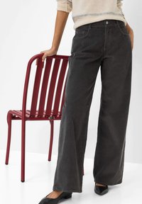 Schwarze Corduroy-Weite-Hosen mit strukturiertem Finish, ausgestattet mit Taschen und einer mittelhohen Taille, kombiniert mit einem roten Metallstuhl.