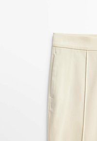 Pantaloni su misura color crema con una texture liscia, design a gamba dritta e tasche laterali. Presentano cuciture ordinate lungo le cuciture.