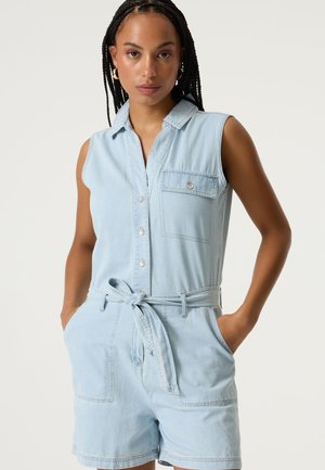 Mono corto de mezclilla azul claro con piernas cortas, diseño sin mangas, botones en la parte delantera y cinturilla ajustable con lazo. Cuenta con un bolsillo en el pecho y detalles sutiles de costura.