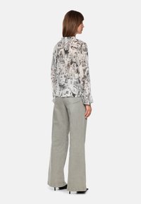 Langärmelige, durchsichtige Bluse mit einem monochromen Stadtansicht-Print, kombiniert mit hochtaillierten, weit geschnittenen grauen Hosen und schwarzen High Heels.