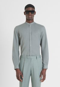 Camicia a maniche lunghe grigio chiaro con colletto a polo, caratterizzata da un ricamo logo discreto, abbinata a pantaloni su misura dello stesso colore. Occhiali da sole inclusi.