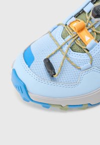 Αθλητικό παπούτσι σε ανοιχτό μπλε χρώμα με πλέγμα και συνθετικό υλικό, υφή επιφάνειας, ενσωματωμένο σύστημα δεσίματος κορδονιών και αντιθετικές πορτοκαλί λεπτομέρειες.