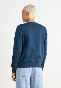 Marineblå sweatshirt med rund hals og ribbede manchetter, lavet af blødt stof; parret med lyseblå høj talje jeans.