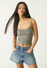Débardeur ajusté vert olive avec de fines bretelles, associé à un short en jean bleu clair taille haute avec un ourlet effiloché et des poches avant.