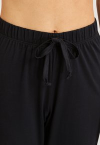 Černé kalhoty na domácí nošení s jemnou texturou, elastickým pasem a detailem vázání vpředu pro nastavitelné nošení.