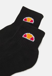 Calcetines negros hasta el tobillo con textura acanalada, que presentan un logo bordado colorido en amarillo, rojo y blanco en el puño.