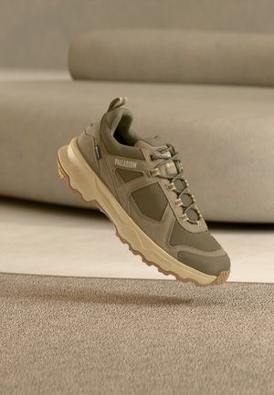 Sneaker Palladium verde oliva con suola beige, tomaia in mesh e camoscio, cuciture dettagliate e lacci in stile trekking, mostrato a mezz'aria su tappeto beige.