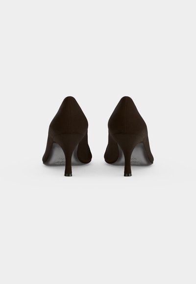 Paire de chaussures à talons noirs vues de dos sur un fond blanc uni.