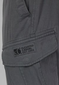 Grijze cargoshorts met een gestructureerde stof, een opvouwbare zak met een logo patch en versterkte stiksels langs de naden.