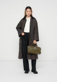 Mørk plaid lang frakke, hvid sweater, sorte bukser og en olivengrøn håndtaske med en stjerneaccent. Glat stof, afslappet pasform og brede ærmer.
