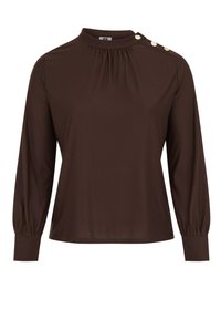 Brūns tops ar garām piedurknēm un augstu apkakli, ar savākta detaļu un trim dekoratīviem pogām uz kreisā pleca. Gluda auduma tekstūra.