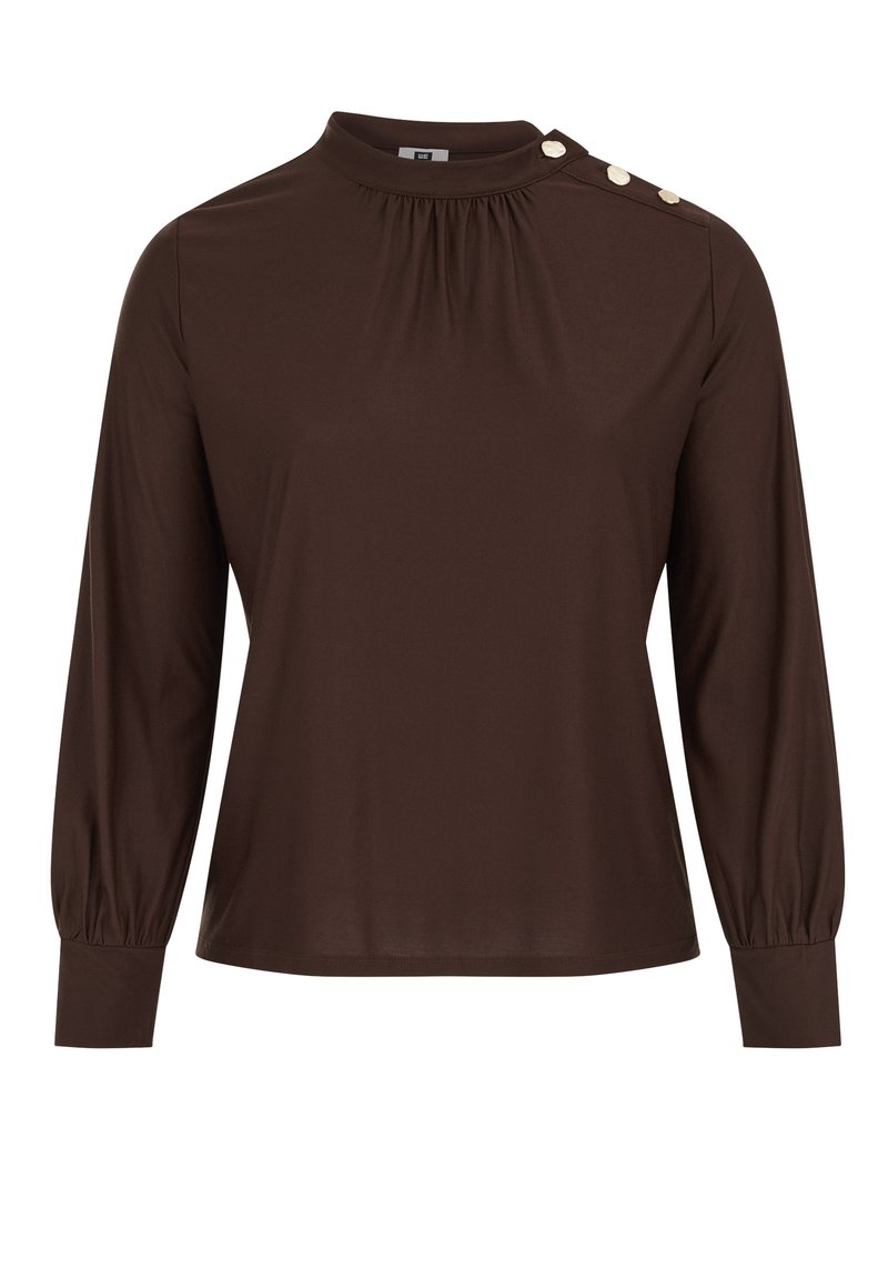 Brūns tops ar garām piedurknēm un augstu apkakli, ar savākta detaļu un trim dekoratīviem pogām uz kreisā pleca. Gluda auduma tekstūra.