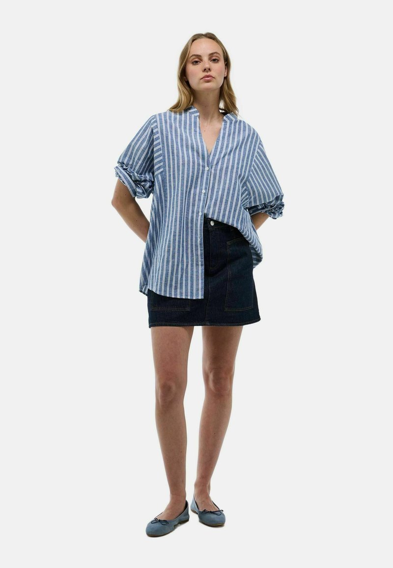 Chemise à boutons bleu et blanc à rayures verticales, manches courtes, associée à une jupe en denim foncé et des ballerines bleues ; tenue décontractée et style relax.