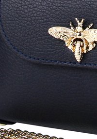 Marine leren tas met een gestructureerd oppervlak, gouden bij-vormige versiering en een gouden kettingriem met een decoratieve rand.