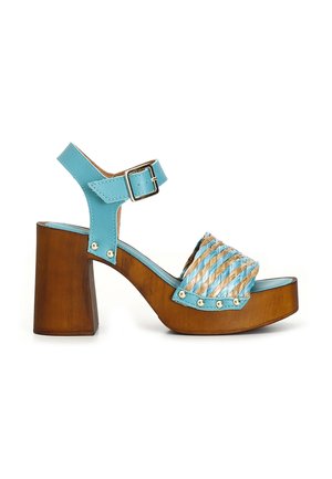 Sandale à plateforme en bois épaisse avec bride de cheville en cuir bleu clair et bride avant tressée bleu et beige avec des clous en métal.