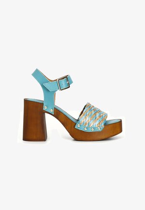 Sandale à plateforme en bois épaisse avec bride de cheville en cuir bleu clair et bride avant tressée bleu et beige avec des clous en métal.