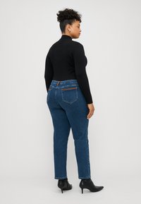 Dark blue jeans with a straight leg design, featuring back pockets and a brown accent on the waistband, paired with a black top and black boots.