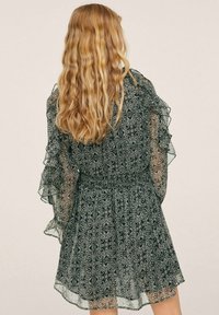 Šifonové šaty černobílé barvy s květinovým vzorem, s volánovými dlouhými rukávy, ustřiženým pasem a plisovanou sukní. Stylizované pro splývavý vzhled.