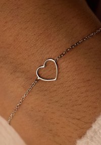 Pulsera de eslabones de plata con una silueta de corazón como punto focal, apoyada sobre piel texturizada. La cadena es delicada, con pequeños eslabones.