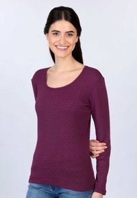 Lila Langarmoberteil mit Rundhalsausschnitt, strukturiertem Muster und weichem Stoff. Kombiniert mit hellblauen Jeans.