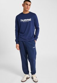 Marinblå långärmad skjorta med vitt logotyp och matchande joggers. Slim fit, mjukt tyg med ribbade mudd och sidologotyp på byxorna.