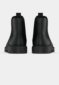 Melns ādas potīšu zābaku pāris ar bieziem gumijas zoliem, redzams no aizmugures uz vienkārša balta fona.