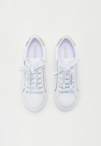 Zapatillas deportivas blancas con un acabado suave, con acentos metálicos dorados, cordones de malla y una suela texturizada. Logo visible en el interior.