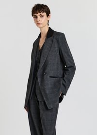 Blazer a quadri grigi con revers in satin nero, design doppiopetto e tasche laterali, abbinato a un gilet coordinato sotto.