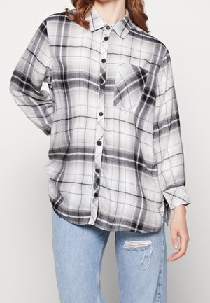 Czarna i biała koszula w kratę na guziki z długimi rękawami, kieszenią na piersi i luźnym krojem, zestawiona z jasnoniebieskimi podartymi dżinsami.