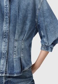 Giacca di jeans di colore azzurro chiaro, con una vestibilità leggermente oversize, maniche a palloncino, polsini elastici e tasche frontali. Tessuto testurizzato con cuciture visibili.
