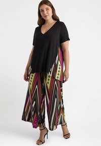 Svart kortärmad topp med V-ringning, i kombination med vida mönstrade byxor med djärva ränder i grön, brun, rosa och krämfärgad.